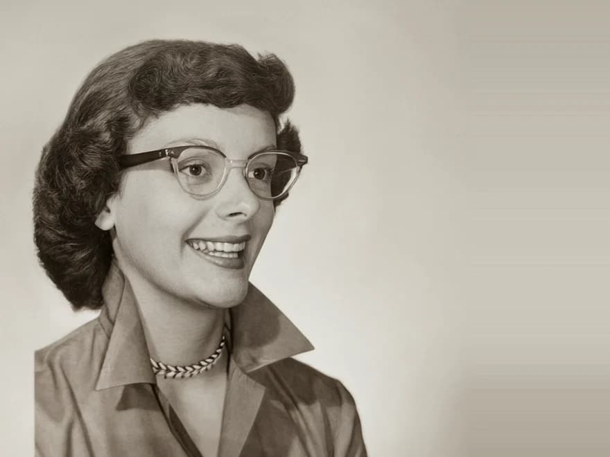 A 1950s studio portrait of a smiling woman in cat-eye glasses, restored
